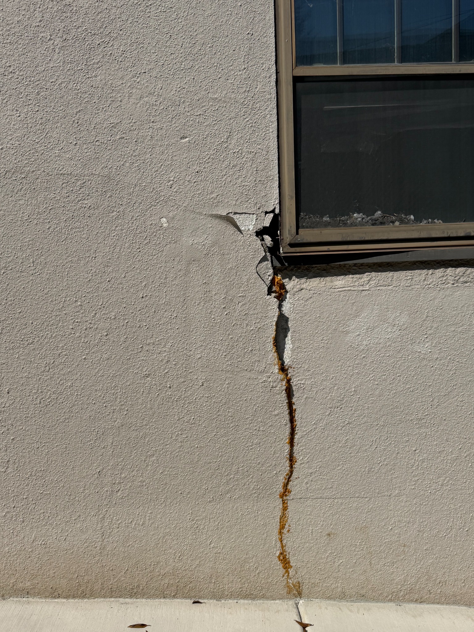 Close view before repair of the deep crack and missing stucco at the window corner