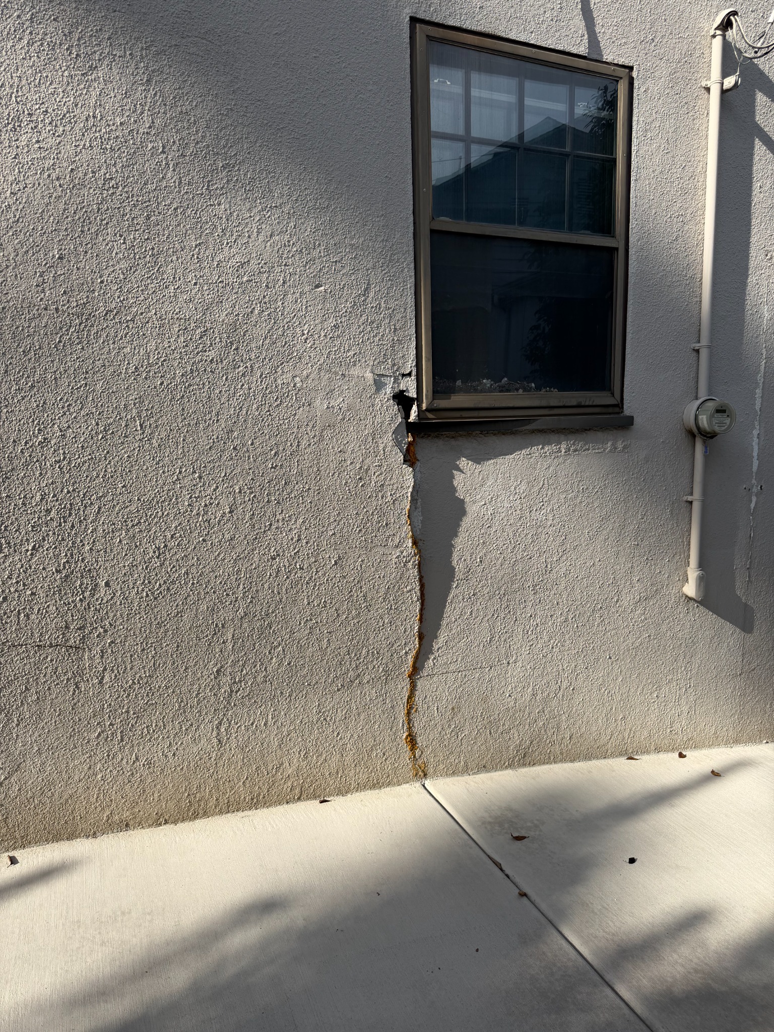 Before repair: cracked and broken stucco beneath the window beside the electric meter